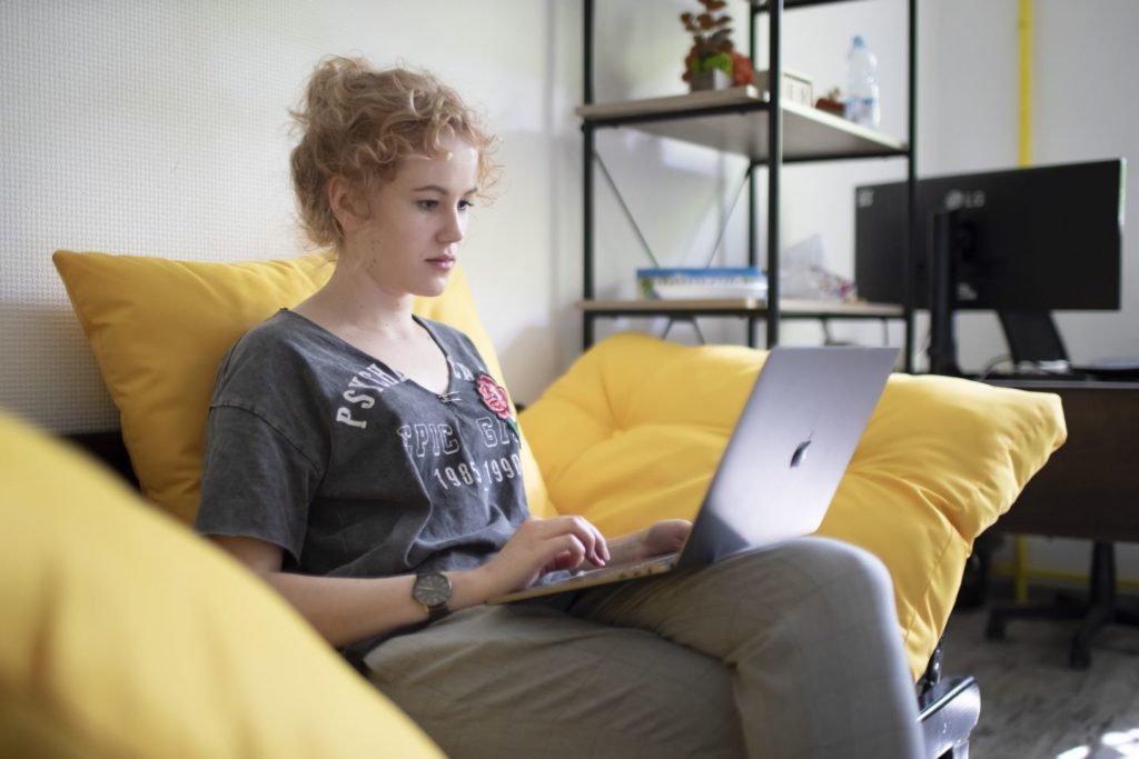A woman sits on the sofa with a laptop