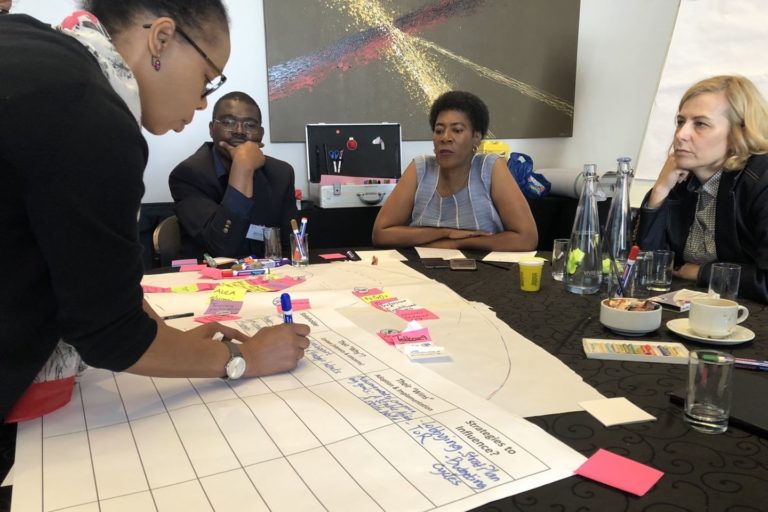 Four people at a table, one of them writes something down