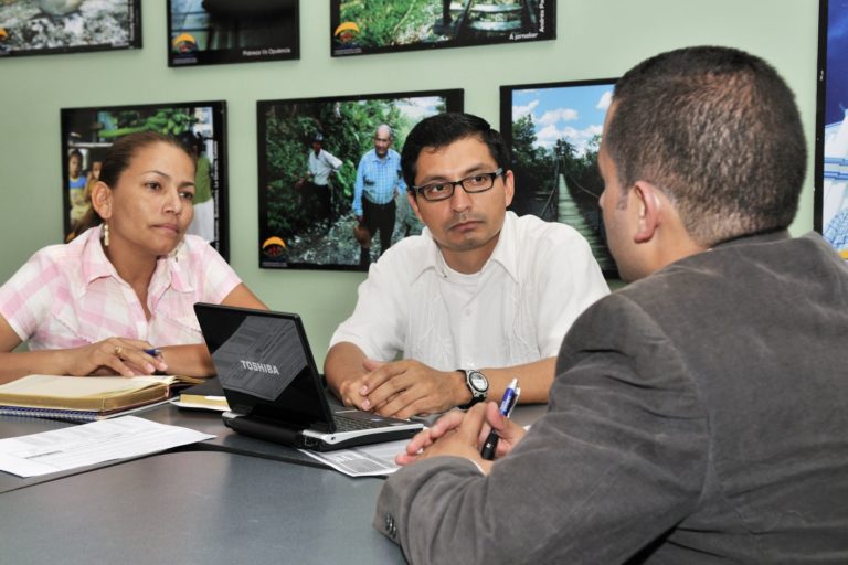 Three people discussing at a table with a computer on it