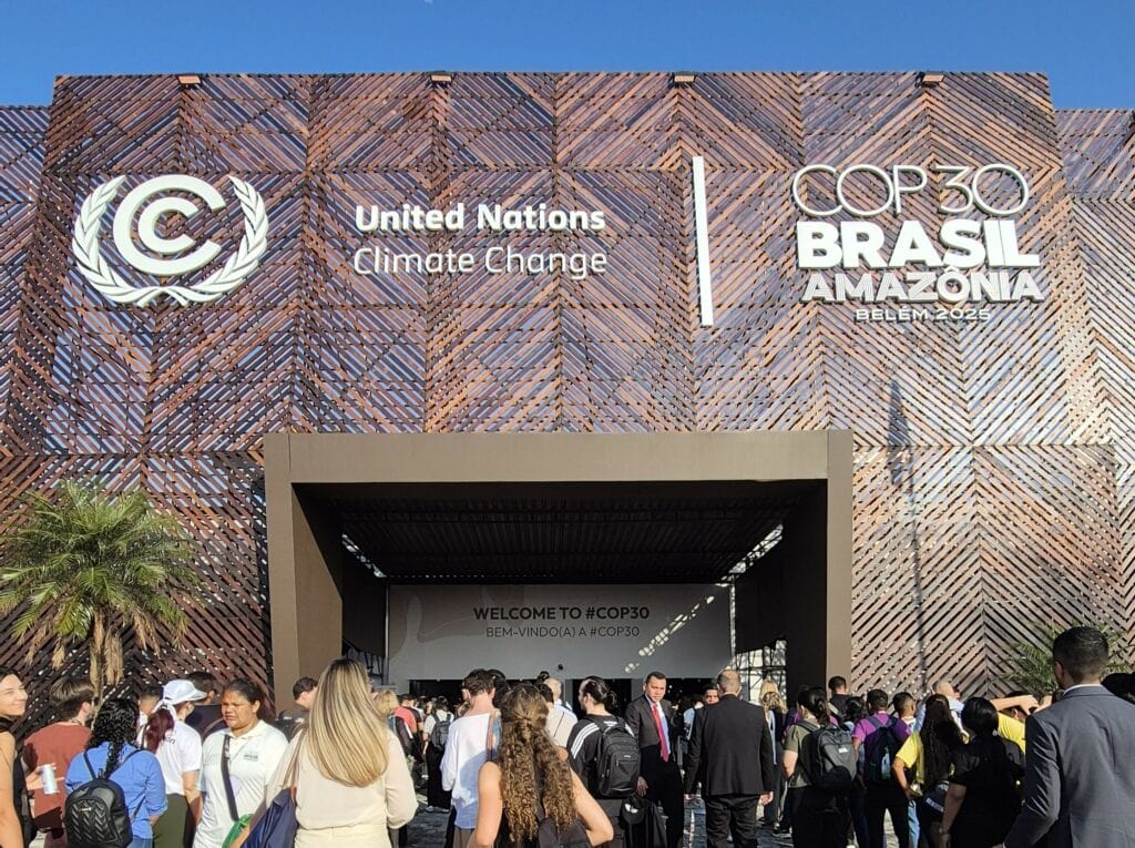 People are walking into the COP30 building on a sunny day.