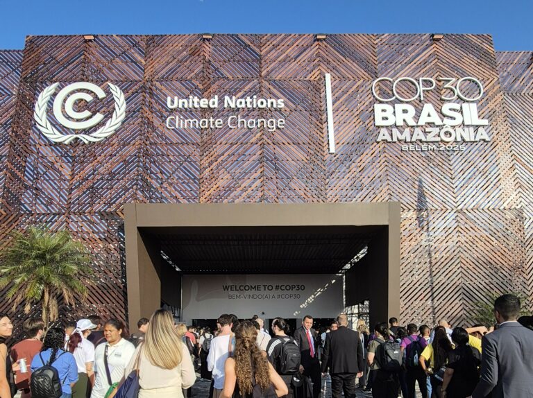 People are walking into the COP30 building on a sunny day.
