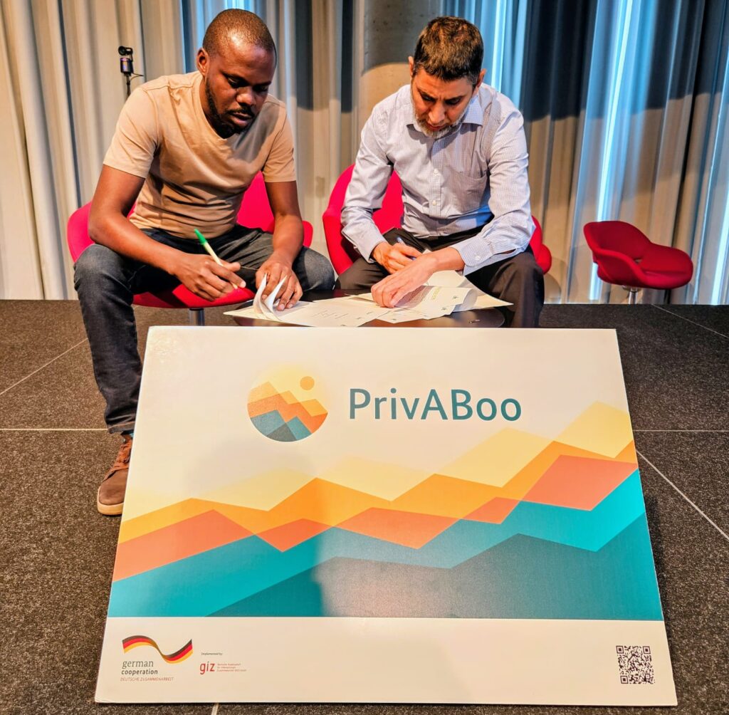 Two men sitting on red chairs at a table, focused on signing documents.
